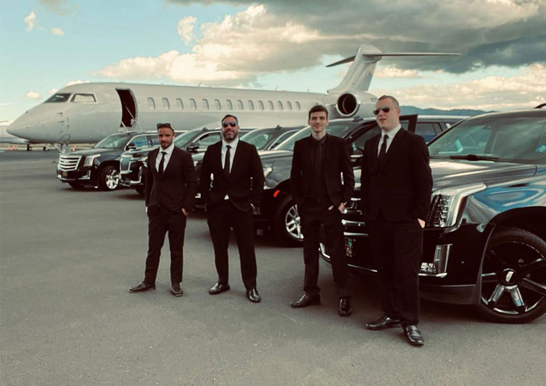 Professional chauffeurs standing beside luxury SUVs and black cars at a private jet center