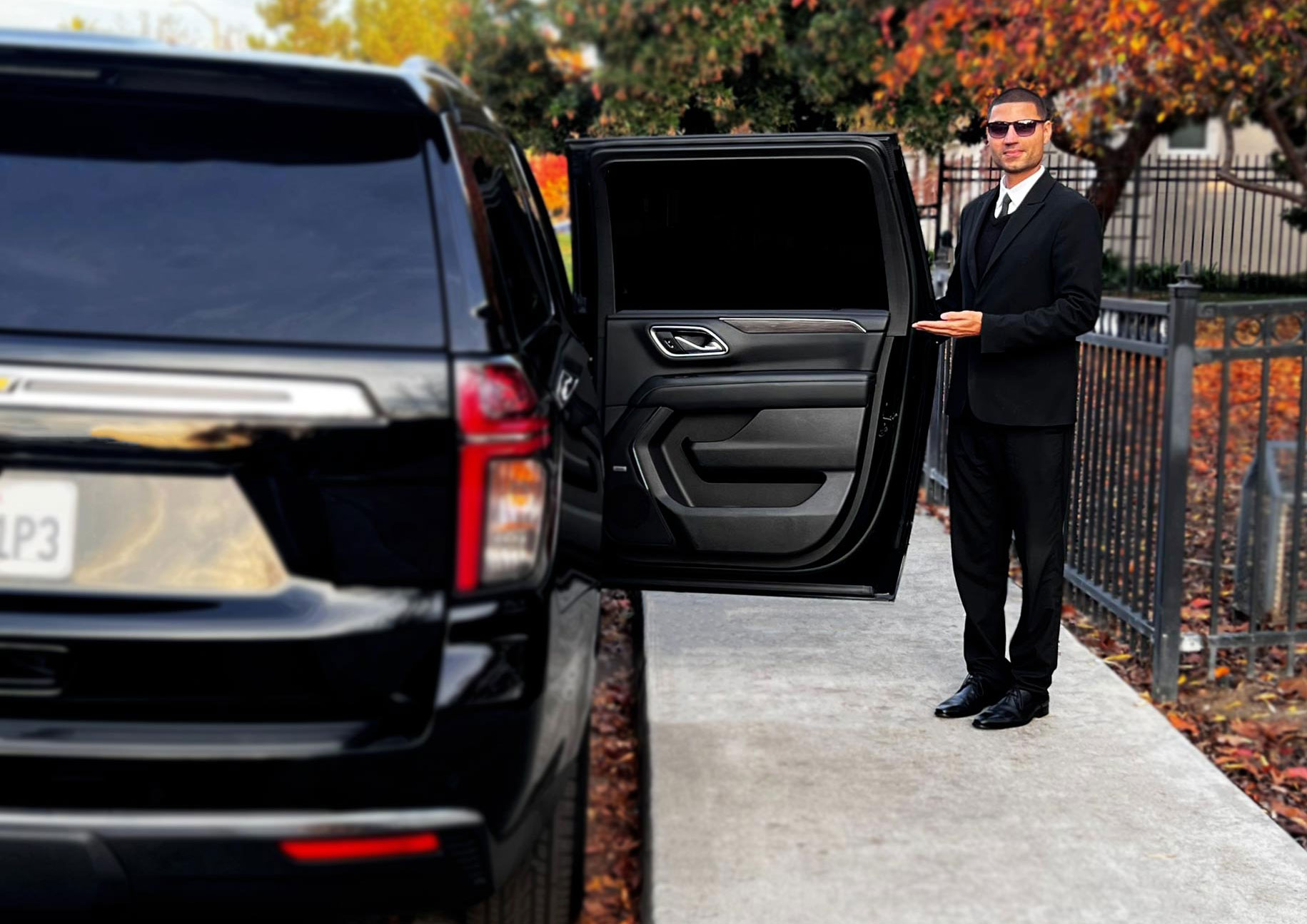 Professional chauffeur in a black suit opening the rear door of a luxury black SUV for airport transportation service in San Francisco