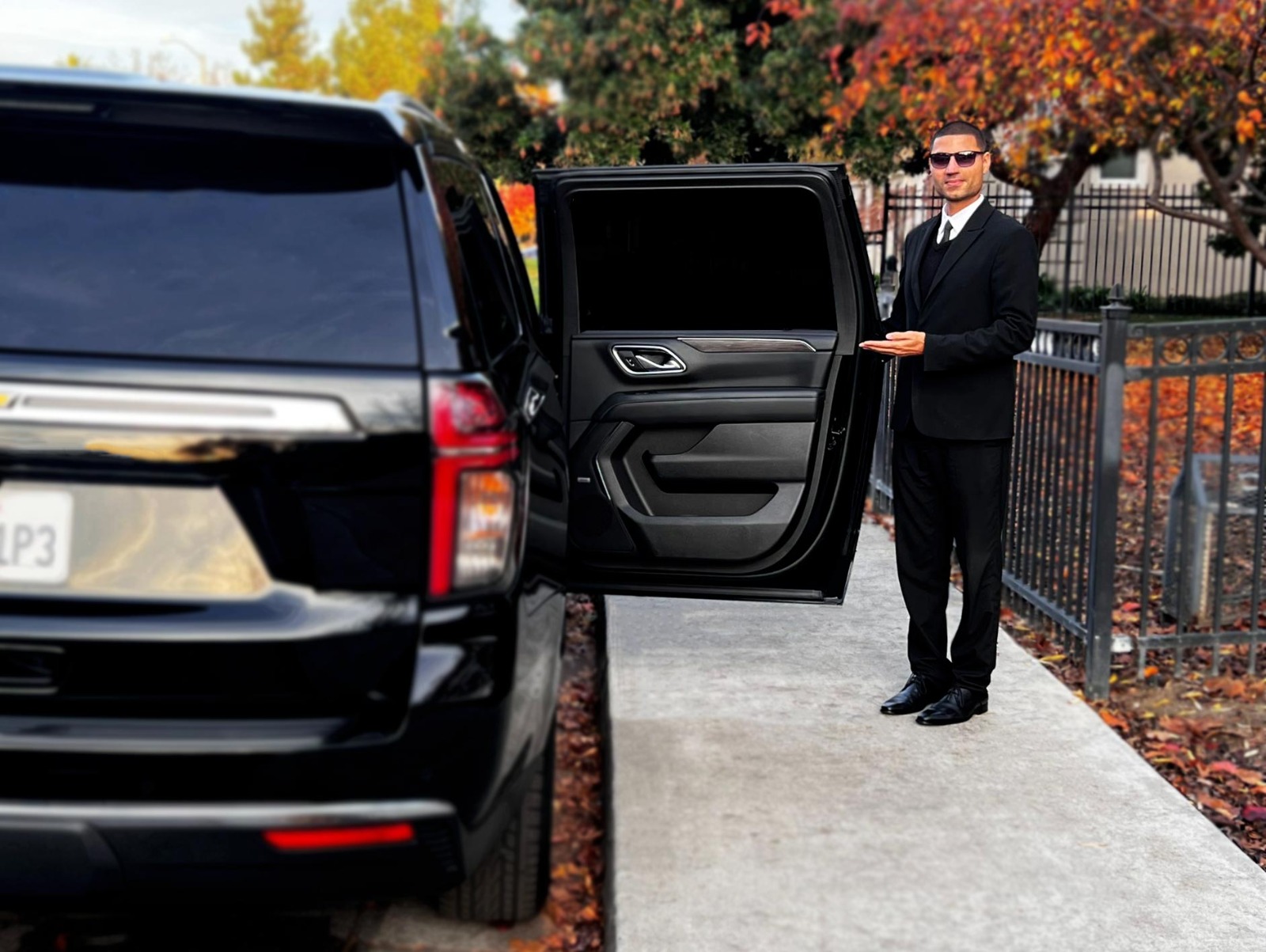 Chauffeur holding the door open beside a black SUV for JFK to White Plains limo service