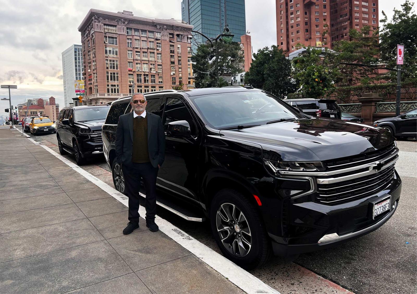 Professional chauffeur standing next to a luxury black SUV in a downtown city environment